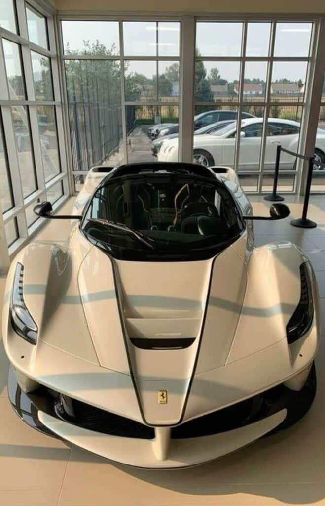 90a9f2b5-2bad-45ae-9ae3-b00c9d63ba88 White sports car displayed in a sunlit showroom with large windows and multiple vehicles in the background. | Sky Rye Design White sports car displayed in a sunlit showroom with large windows and multiple vehicles in the background.