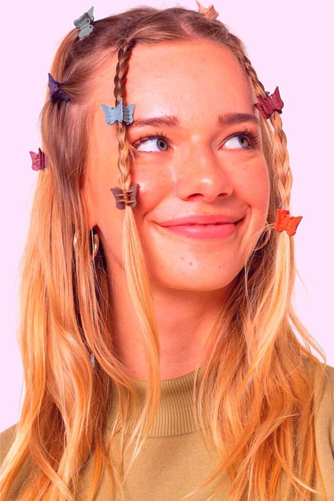 Smiling woman with braided hair and colorful butterfly clips against a pink background.