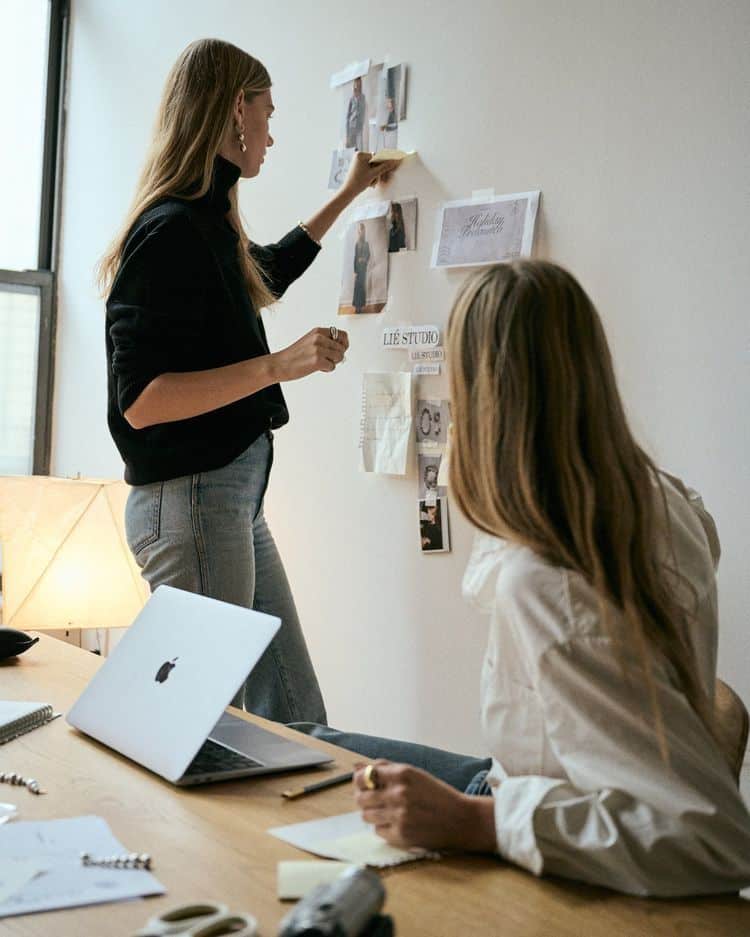 Two women collaborating on a creative project, using a mood board and laptop in a modern office setting.