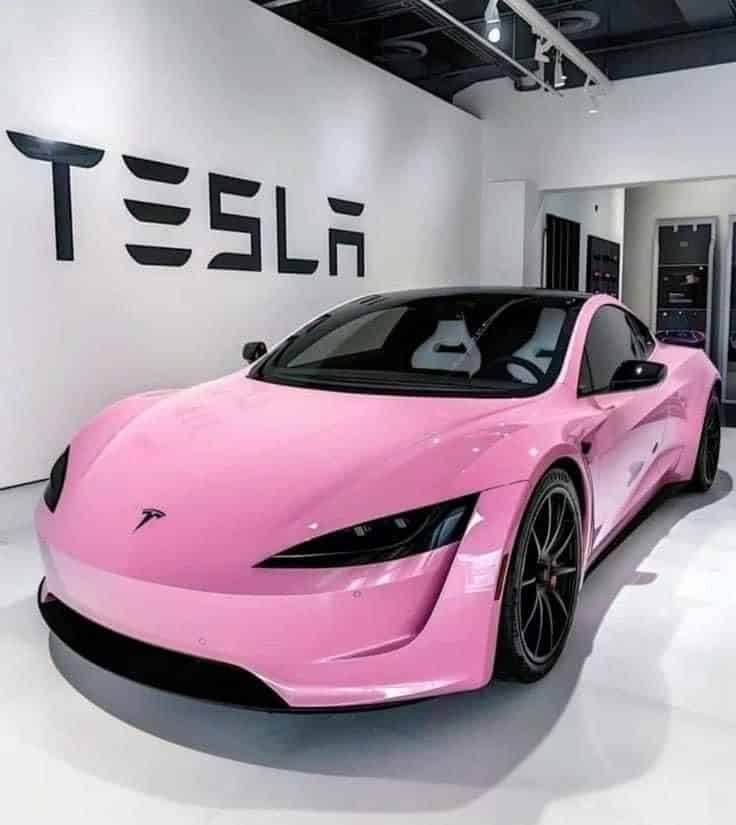 Pink Tesla sports car showcased in a showroom with the Tesla logo in the background.