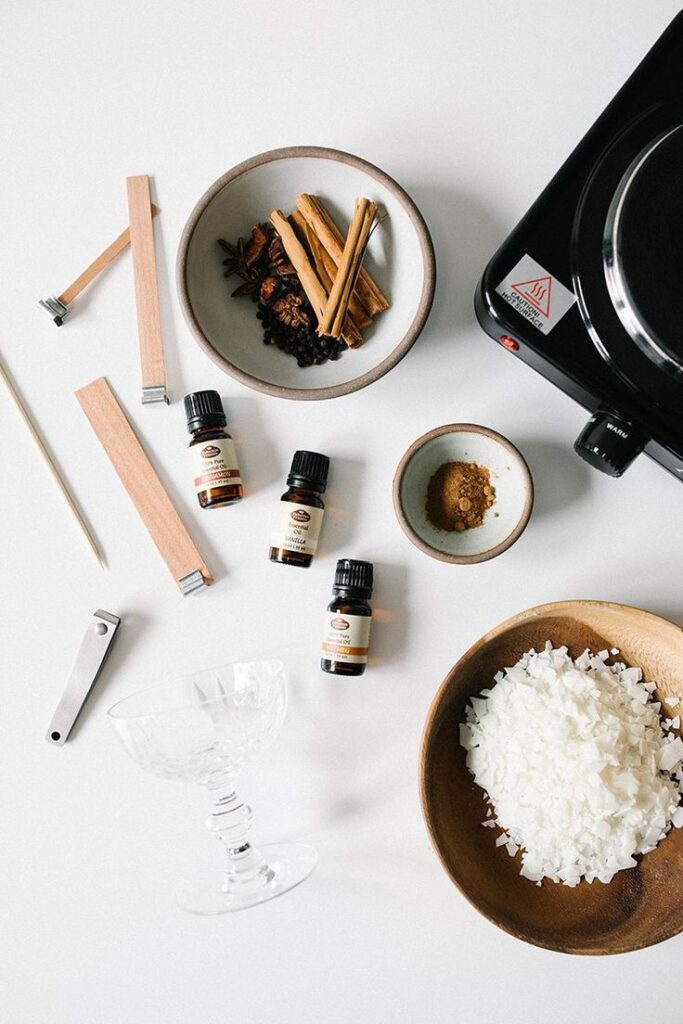 Candle-making supplies and spices on a table: oils, wicks, wax, cinnamon, and a hot plate for DIY projects.
