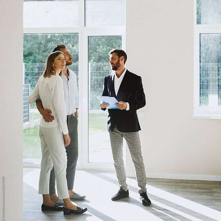 Real estate agent showing couple a bright, empty room in a house.