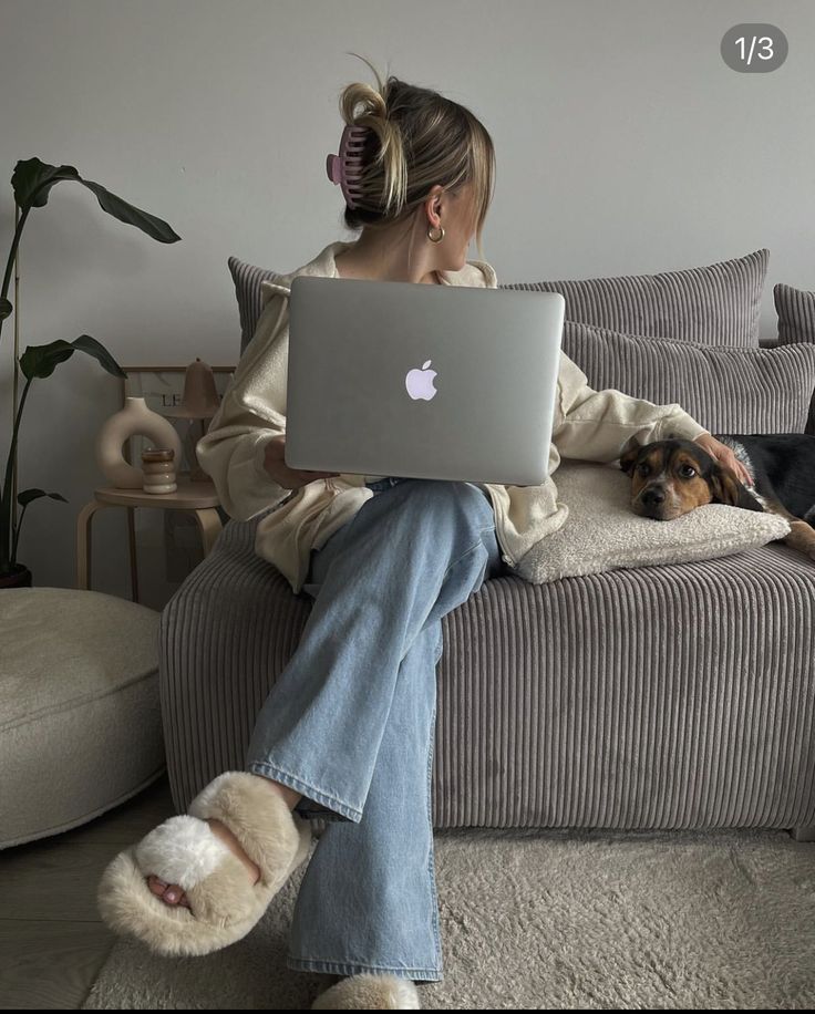 Woman working on a laptop with a dog on the couch, cozy casual home setting.