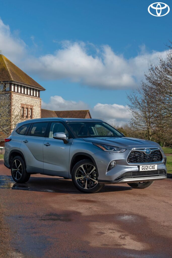 Silver Toyota SUV parked on a country road with a house and cloudy blue sky in the background.