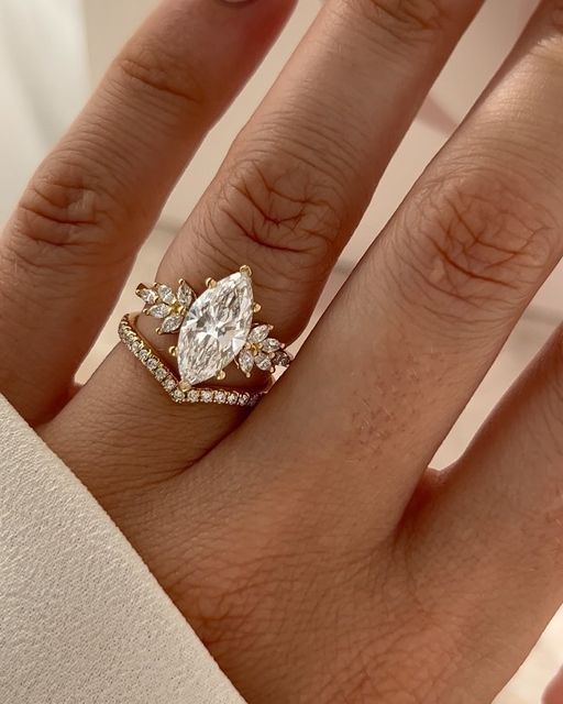 Elegant marquise diamond ring with floral design on a hand, featuring gold and sparkling accent stones.