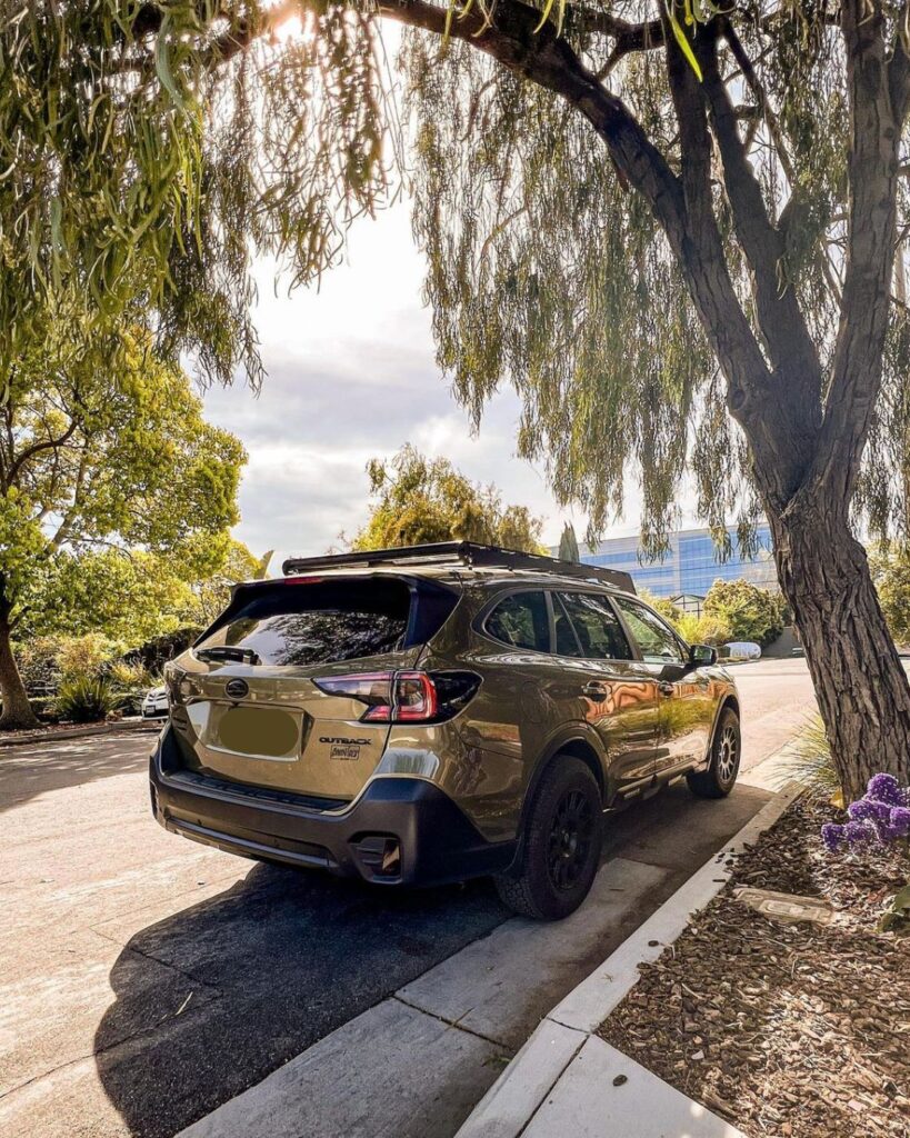 SUV parked under a tree on a sunny day, with cityscape in the background and sunlight filtering through branches.