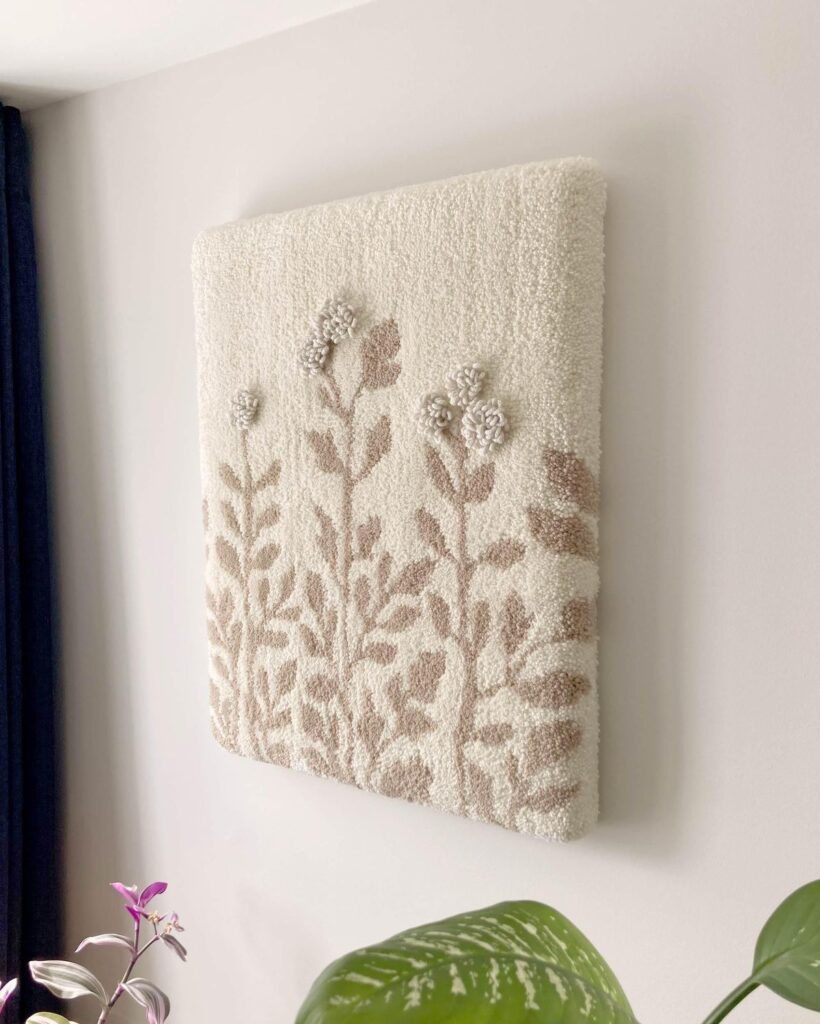 Floral beige wall art with textured design on light background, surrounded by greenery accents.
