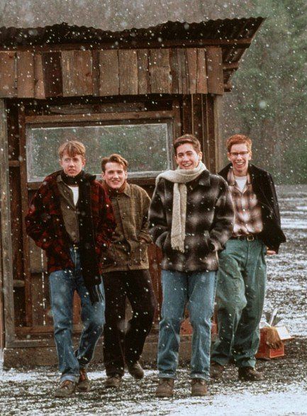 Group of friends walking and smiling in snowy weather outside a wooden cabin, wearing winter clothes.