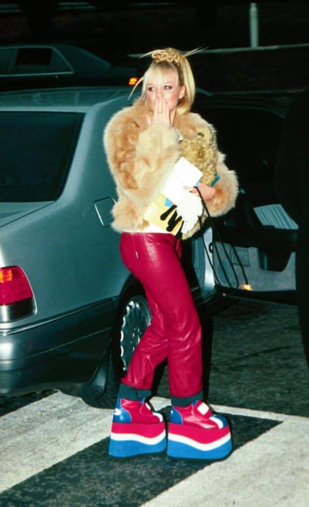 Person in fur coat and red leather pants with platform shoes exiting car, covering mouth playfully.