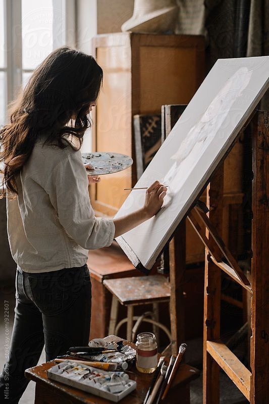 Artist painting on canvas in a cozy studio, with brushes and palette in hand.