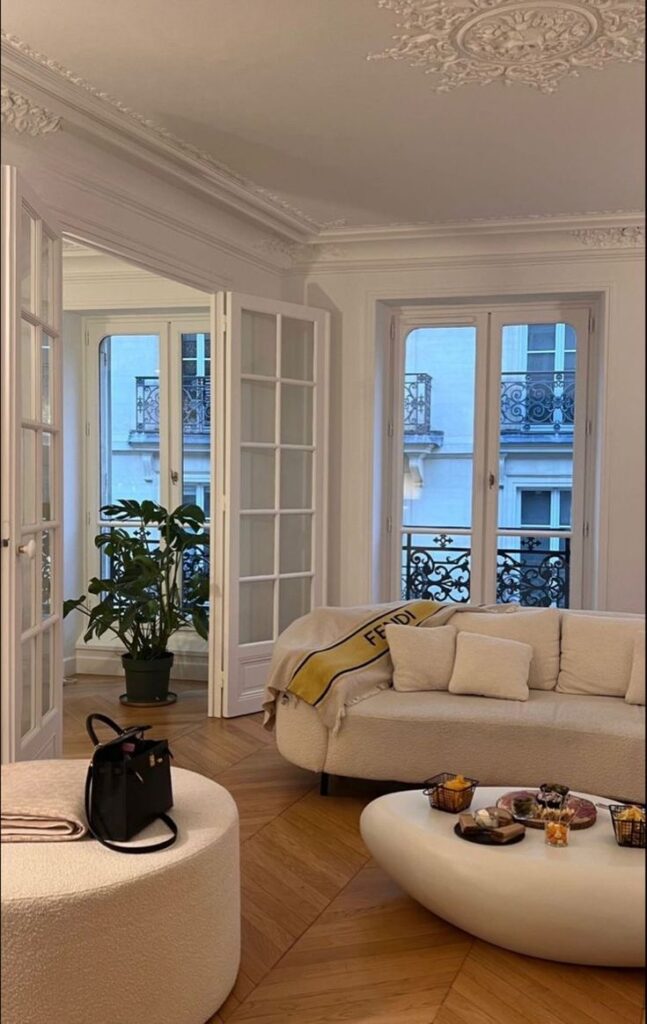 Elegant living room with chic decor, open French doors, ornate ceiling, hardwood floor, and cozy sofa.