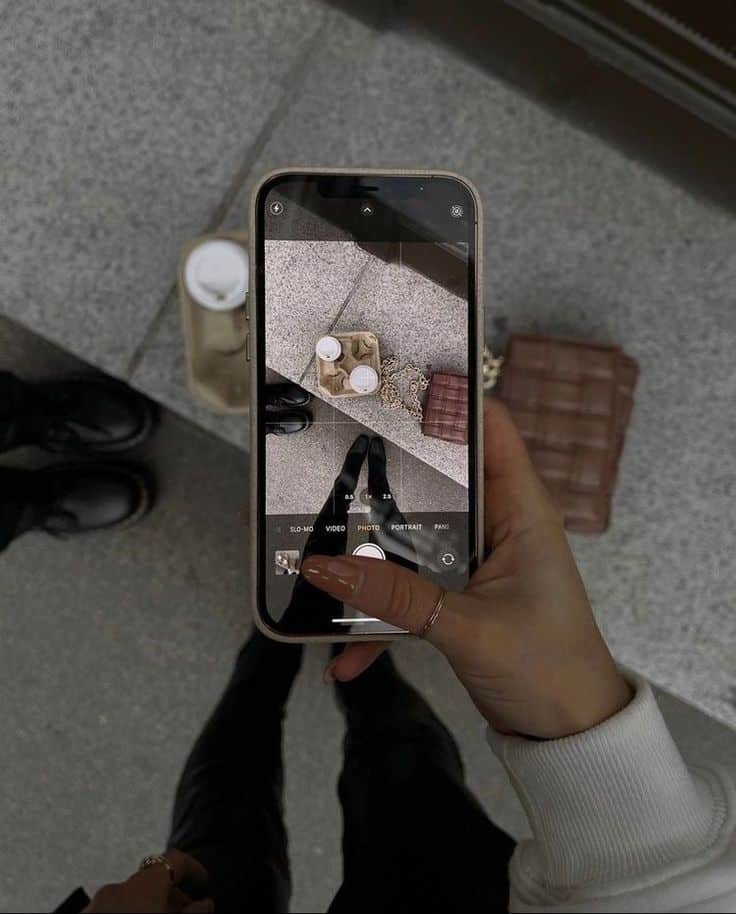 Person photographing coffee and bag on smartphone, urban street style scene.