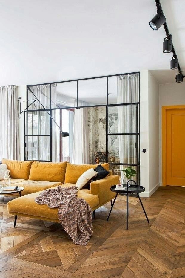Modern living room with mustard sofa, glass wall, and geometric wood flooring. Cozy and stylish interior design.