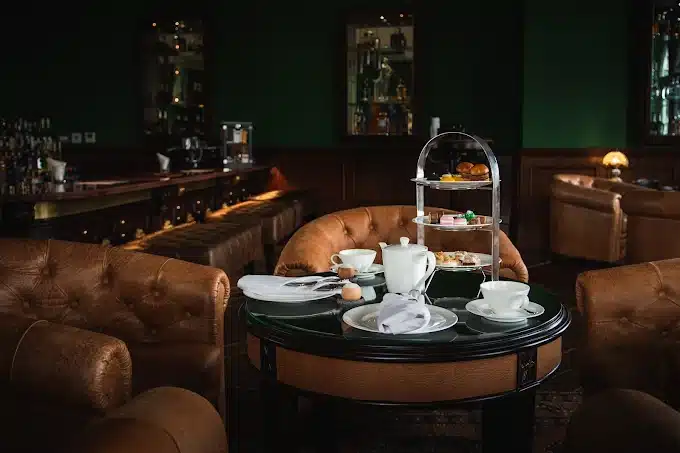Elegant afternoon tea setup in a cozy, dimly-lit lounge with pastries, tea set, and plush leather seating.