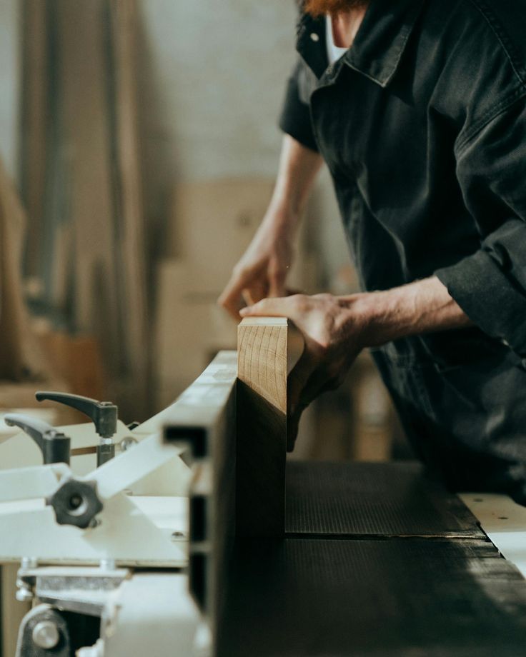 Carpenter shaping wood plank with a planer in a workshop.