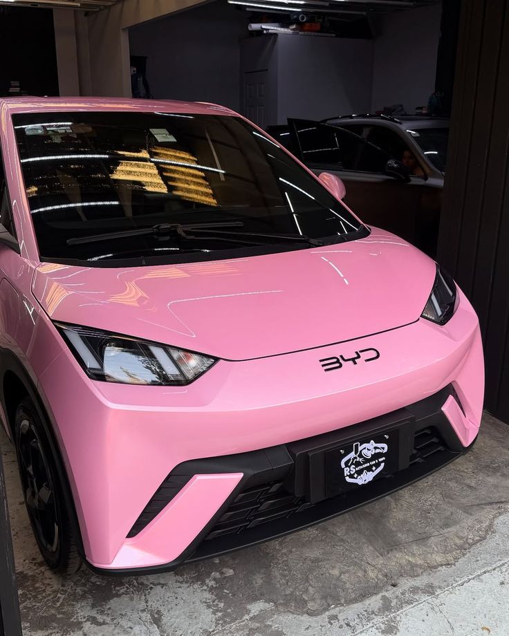 Pink BYD compact car parked in garage, front view with sleek design and modern headlights.