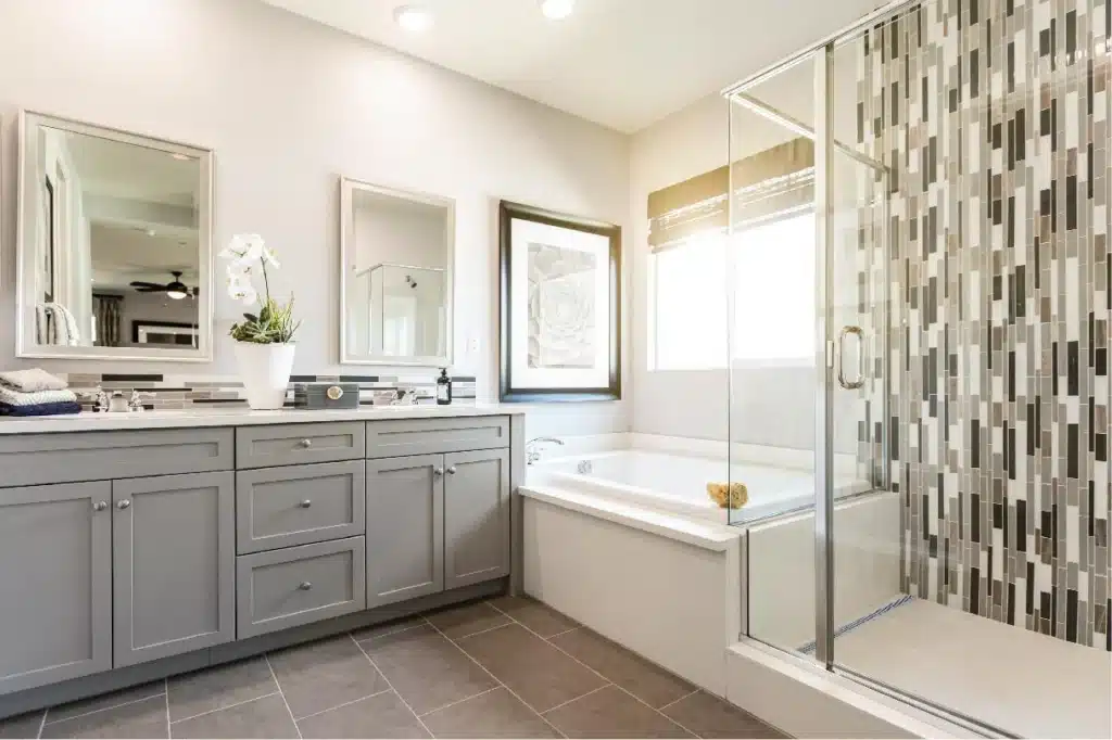Modern bathroom with gray cabinets, glass shower, and tub featuring stylish mosaic tiles.