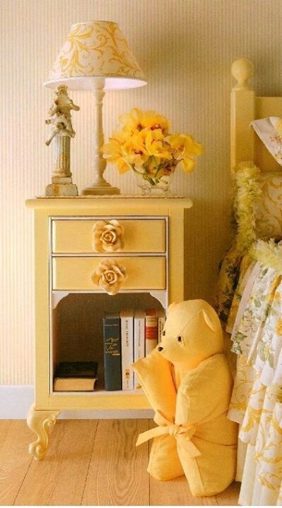 Yellow nightstand with floral lamp, book selection, and cozy bear enhancing a warm, inviting bedroom ambiance.