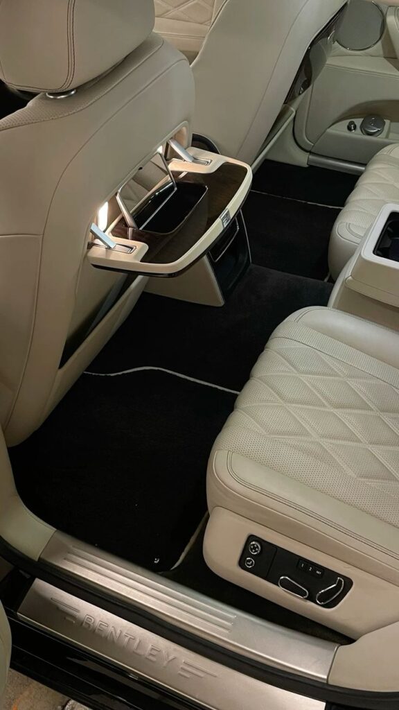 Luxury car interior with beige leather seats, wooden tray tables, and Bentley branding.