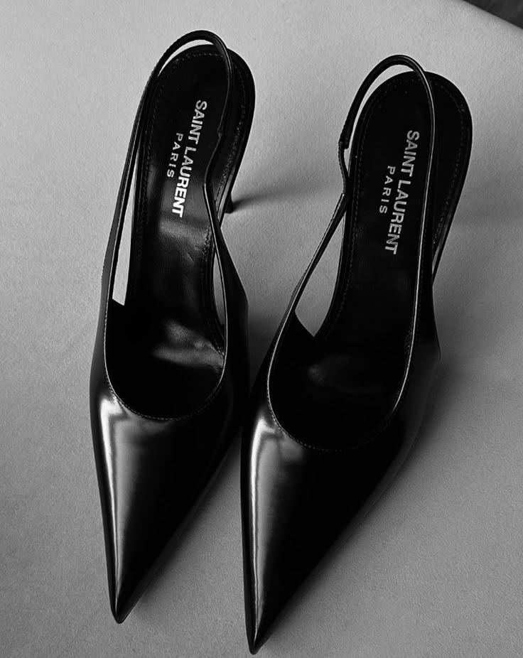 Elegant black leather Saint Laurent slingback heels with pointed toes on a grey background.