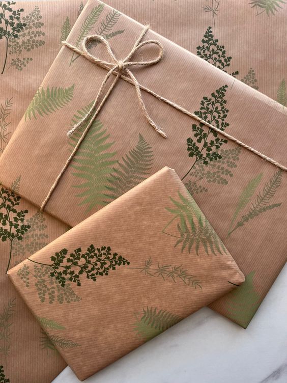 Gift boxes wrapped in botanical-themed brown paper with green fern prints and tied with twine.