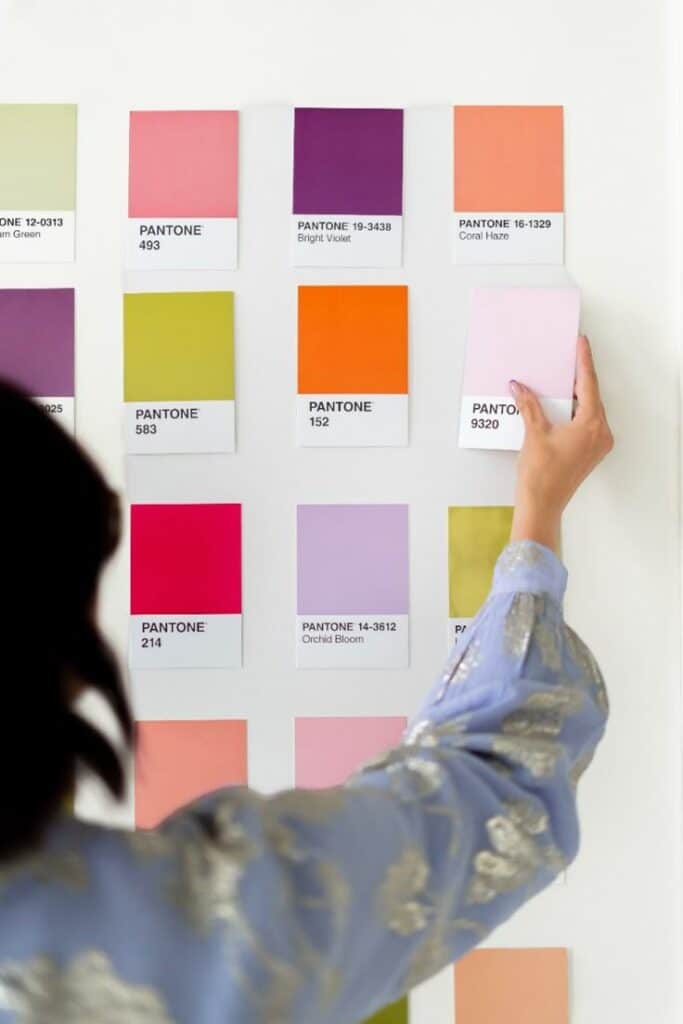 Person arranging Pantone color swatches on a wall, showcasing vibrant hues like violet, coral, and lime.
