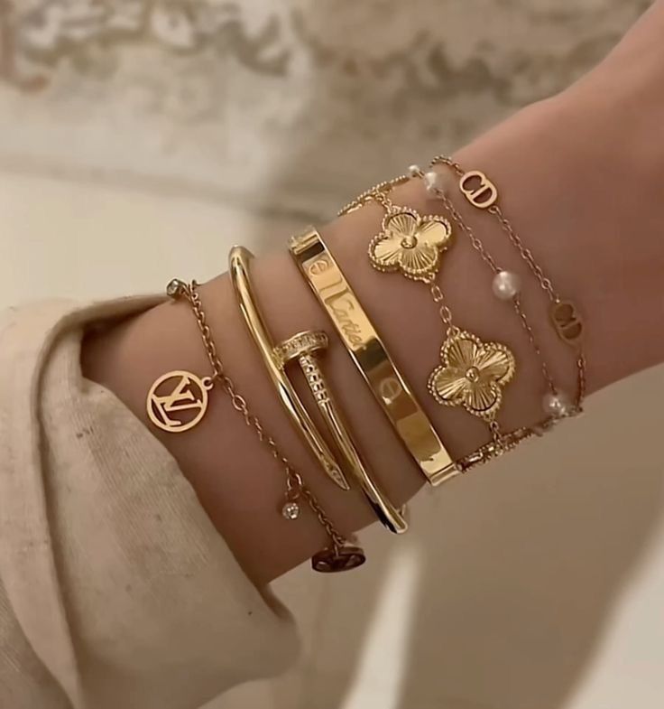 Stylish gold and charm bracelets stacked on a wrist, featuring delicate floral and nail designs.