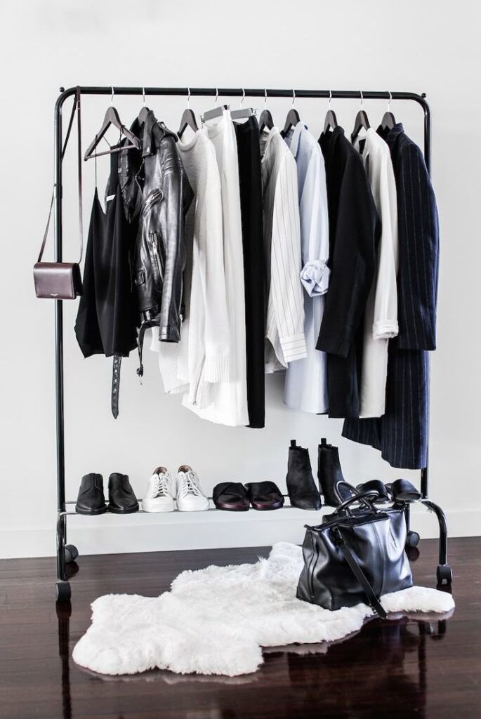 Minimalist wardrobe with black and white clothes, shoes, and accessories on a rack over a white rug.