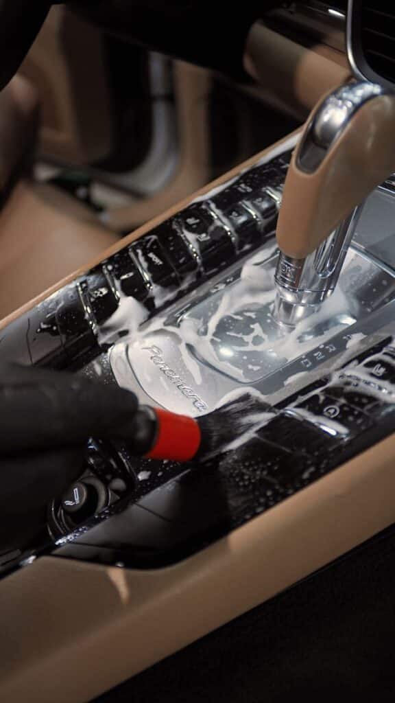 Cleaning luxury car interior console with detailing brush and foam for thorough maintenance.