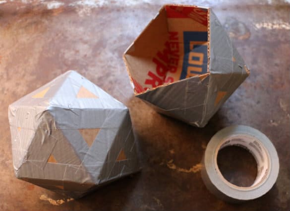 DIY geometric shapes made with cardboard and duct tape, next to a roll of tape on a rustic surface.