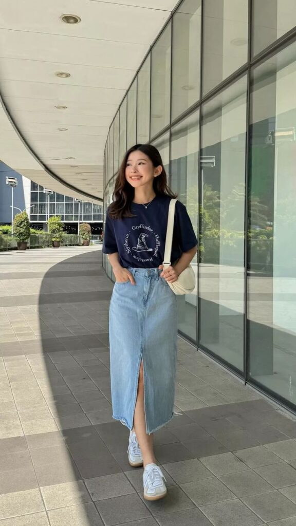 Young woman in casual outfit walking in an urban setting, wearing a graphic tee and denim skirt, smiling in the sunshine.