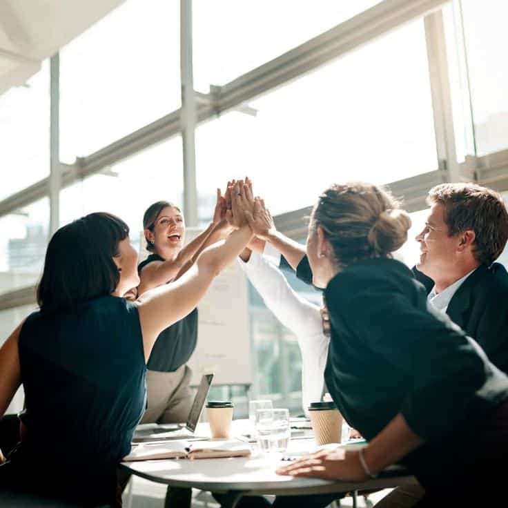 Team celebrating success with a group high-five in a bright office setting.