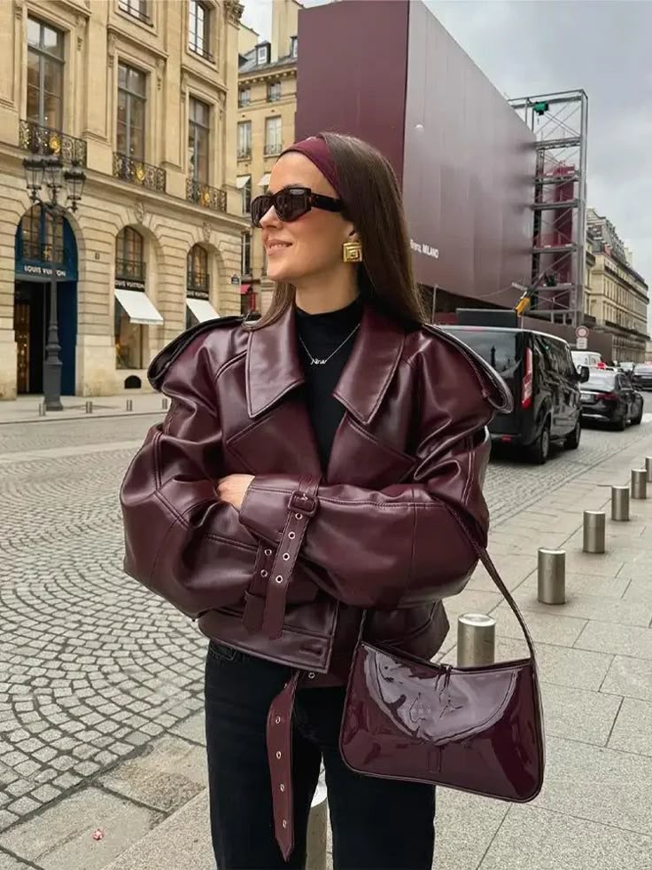 Stylish woman in burgundy leather jacket and sunglasses, standing on a Paris street with chic purse and headband.