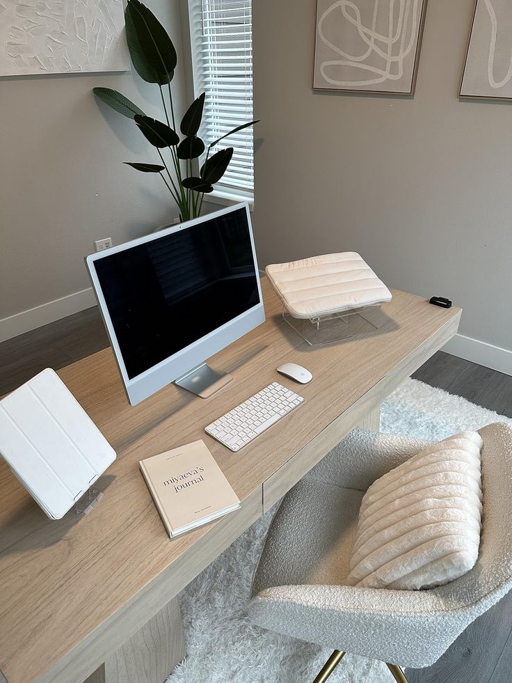 Modern home office setup with computer, keyboard, and stylish chair. Minimalist decor and lush plant by the window.