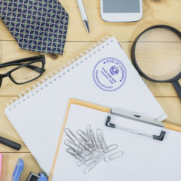 Office desk with a notebook, glasses, phone, and magnifying glass. Features a Louisiana engineering geologist's seal.