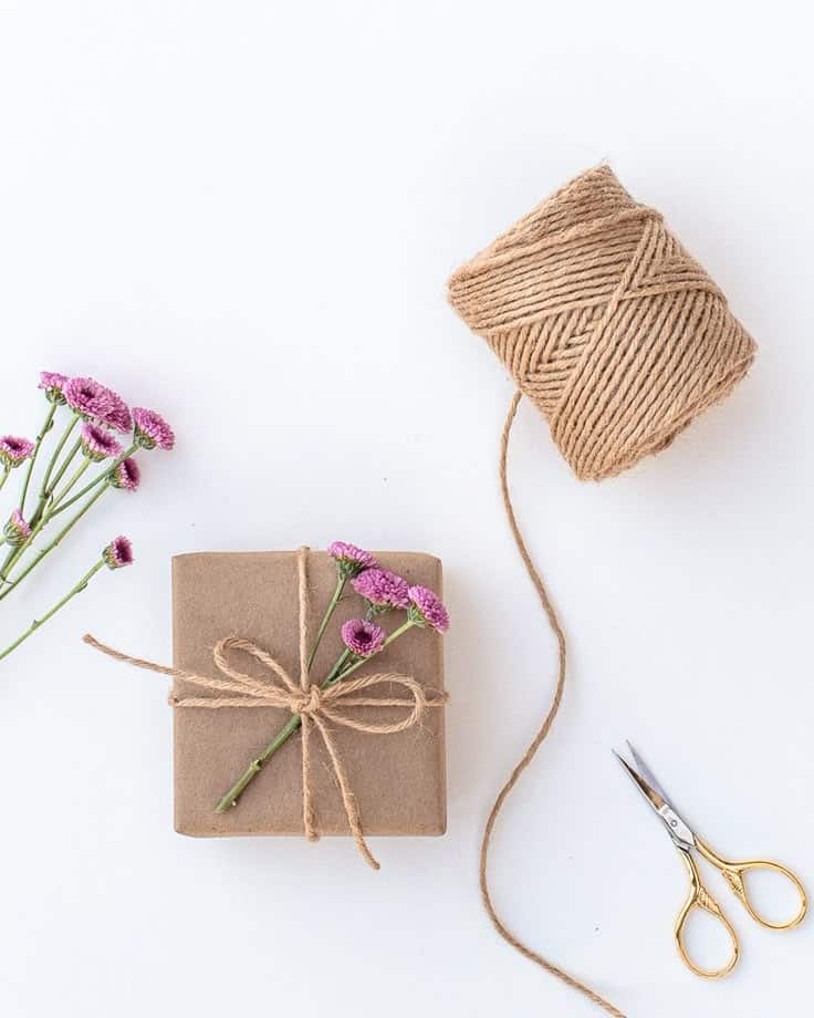 Gift wrapped in brown paper with twine, purple flowers, and scissors. Eco-friendly packaging concept.