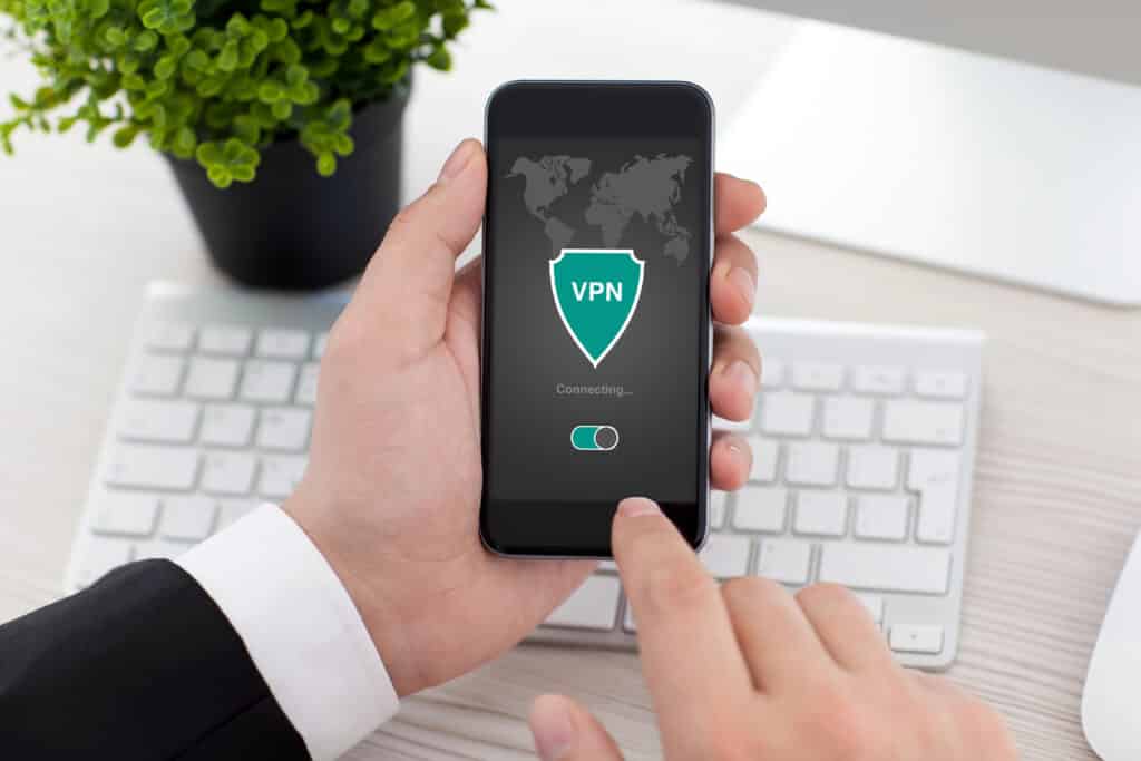 Depositphotos_142620117_XL Person holding smartphone with VPN app connecting on screen, near keyboard and plant. Secure internet browsing concept. | Sky Rye Design Person holding smartphone with VPN app connecting on screen, near keyboard and plant. Secure internet browsing concept.