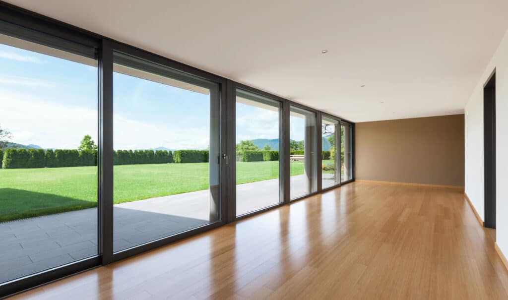 Depositphotos_178659190_XL Spacious modern room with large windows, wooden flooring, overlooking a lush green backyard and clear blue sky. | Sky Rye Design Spacious modern room with large windows, wooden flooring, overlooking a lush green backyard and clear blue sky.