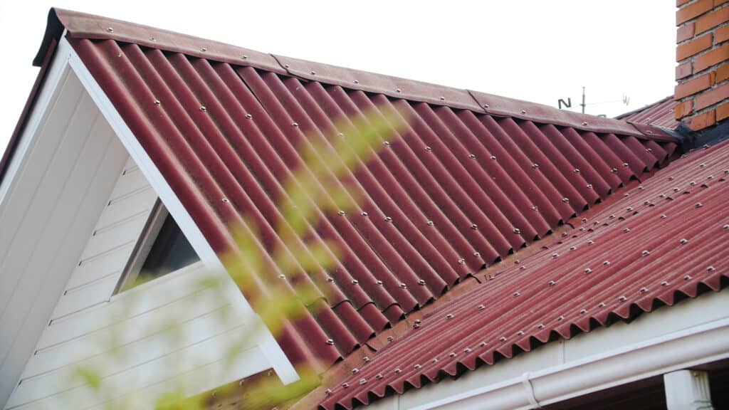 Red corrugated metal roof with a white house facade and chimney stack.