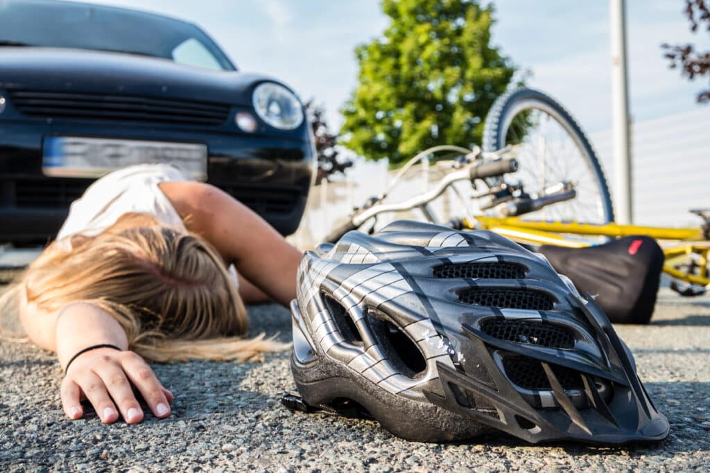 Bicycle accident scene with fallen cyclist and helmet near a car, emphasizing road safety and cycling protection.