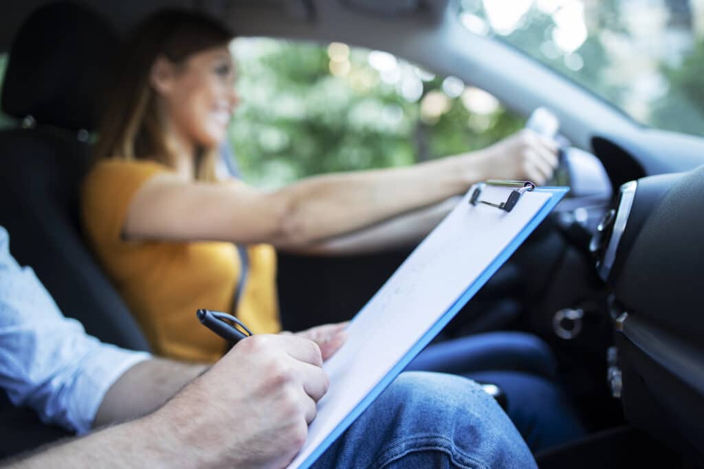 Person taking a driving test, instructor with clipboard, learner at the wheel, inside car.
