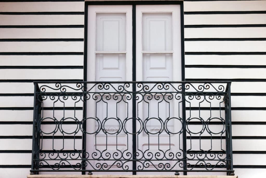 Black iron balcony railing against white striped wall.