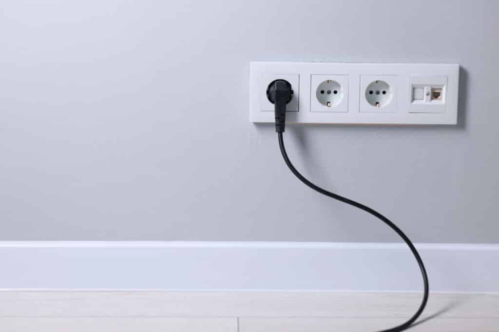 Power outlet on gray wall with one black plug inserted.