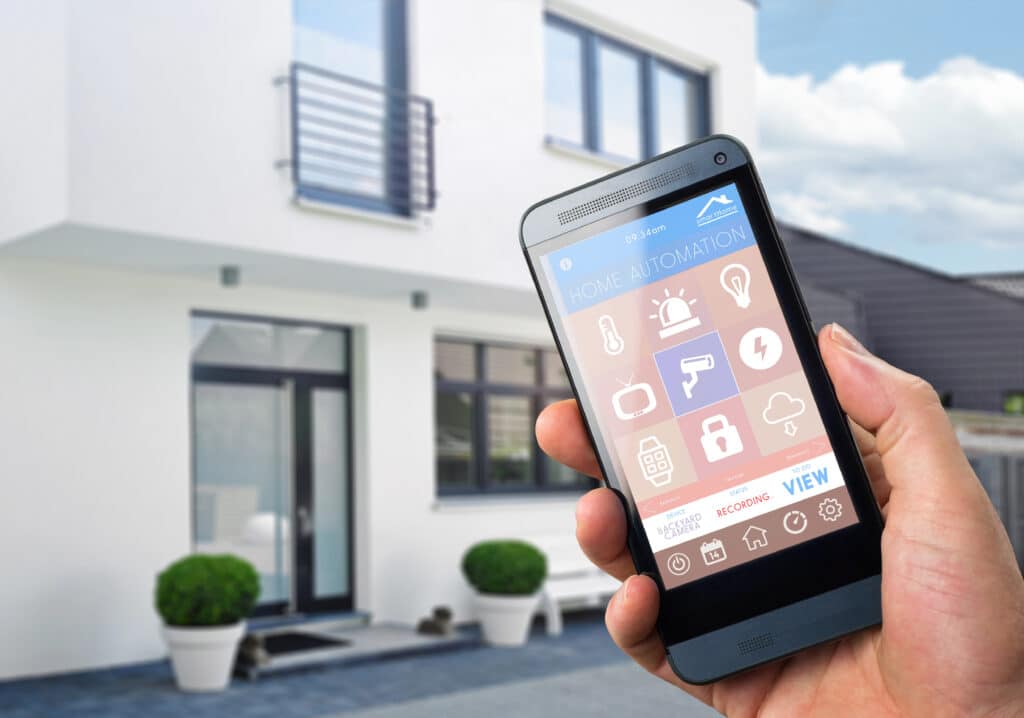 Person using smartphone home automation app in front of modern house.