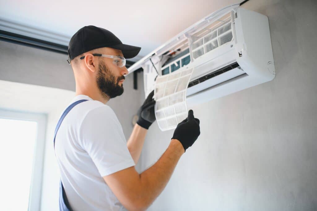 Technician servicing an air conditioner, wearing safety gear and gloves, changing the filter for maintenance.