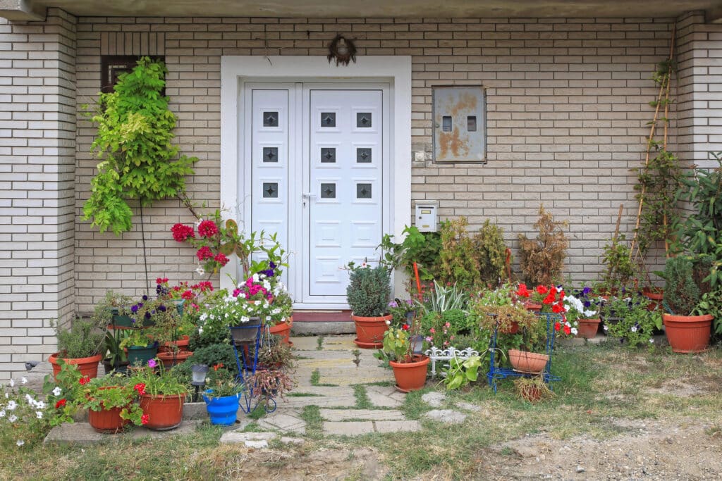 White front door with vibrant potted plants on concrete steps, enhancing brick house entrance with colorful garden decor.