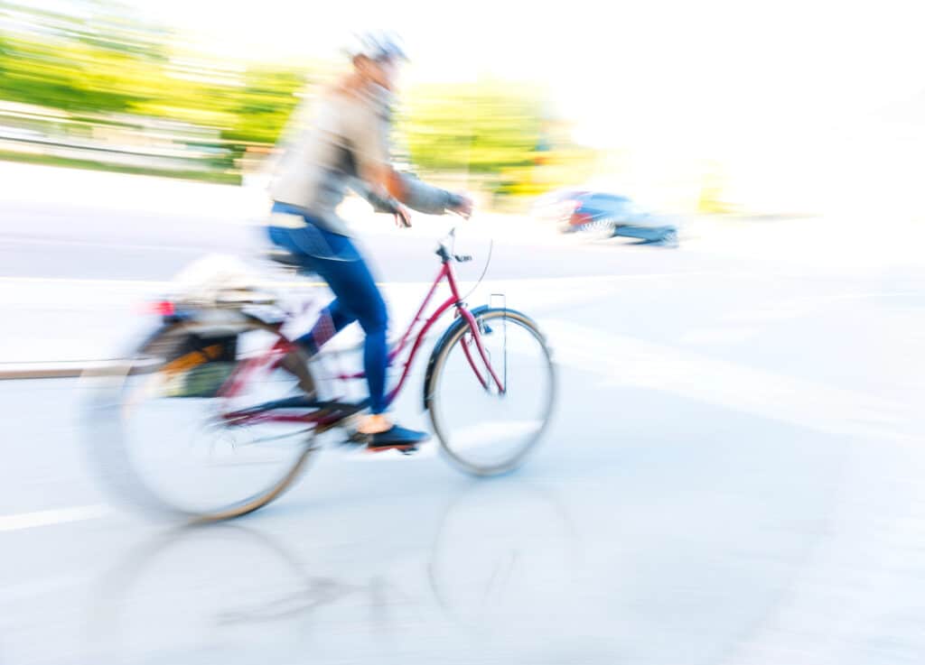 Blurry image of a cyclist riding a bike on a sunny urban street, conveying speed and motion.