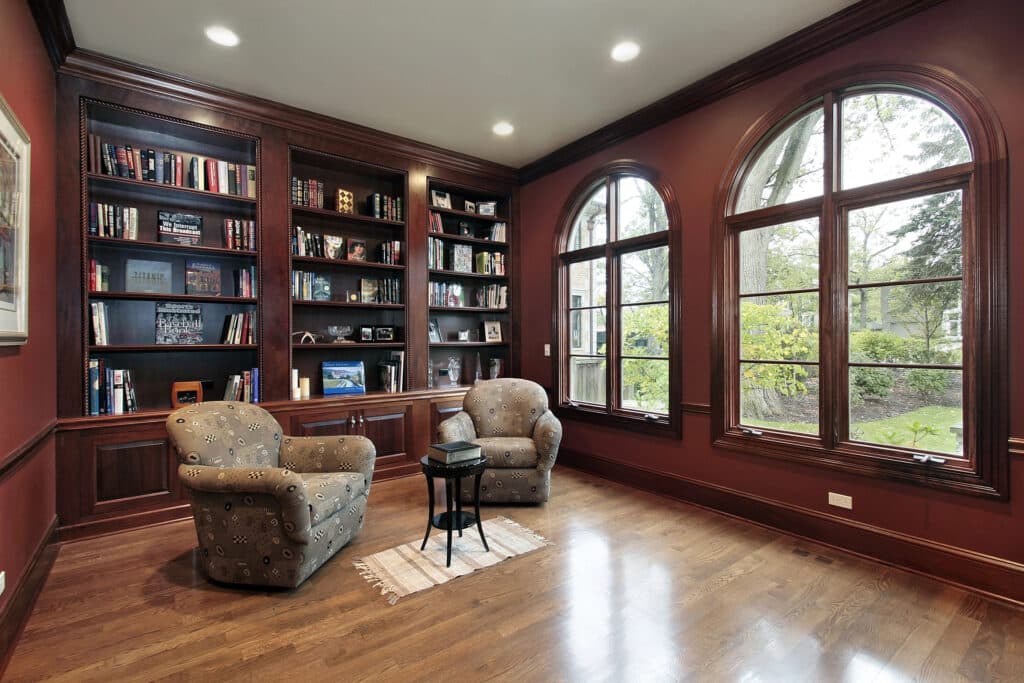 Cozy home library with plush chairs, bookshelves, and large arched windows overlooking a garden.