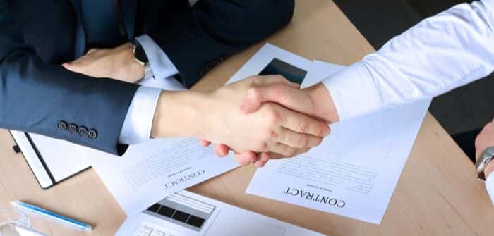 Business handshake over contract papers on desk, symbolizing partnership and agreement in a professional setting.