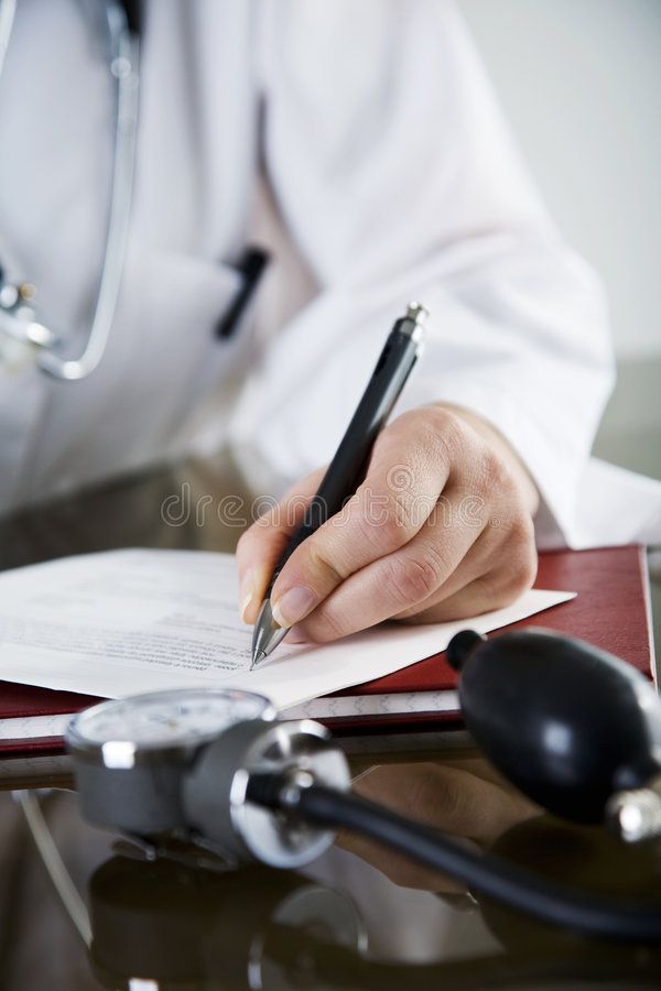 Doctor writing a prescription with a stethoscope and blood pressure monitor on the table.